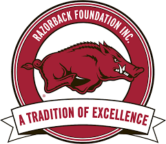 The Razorback Foundation Inc. logo. The hog is in the center of a red circle which says "Razorback Foundation Inc." and there is a white banner across the bottom part o the circle that says "A Tradition of Excellence."