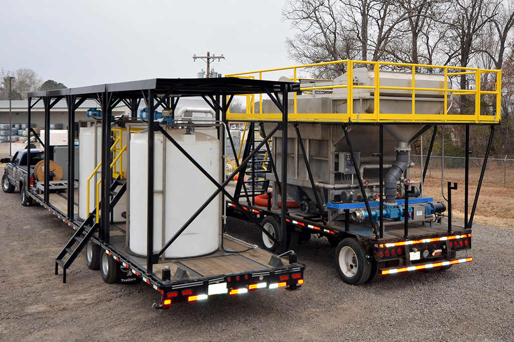 Trailers carrying Water Tech rental equipment. One trailer has two large white tanks and the other has one metal processing tank.