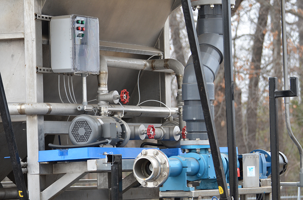 A piece of Water Tech rental equipment for wastewater treatment. A short piece of light blue pipe has a plastic gray tube sticking out of the top and connecting into the system above.