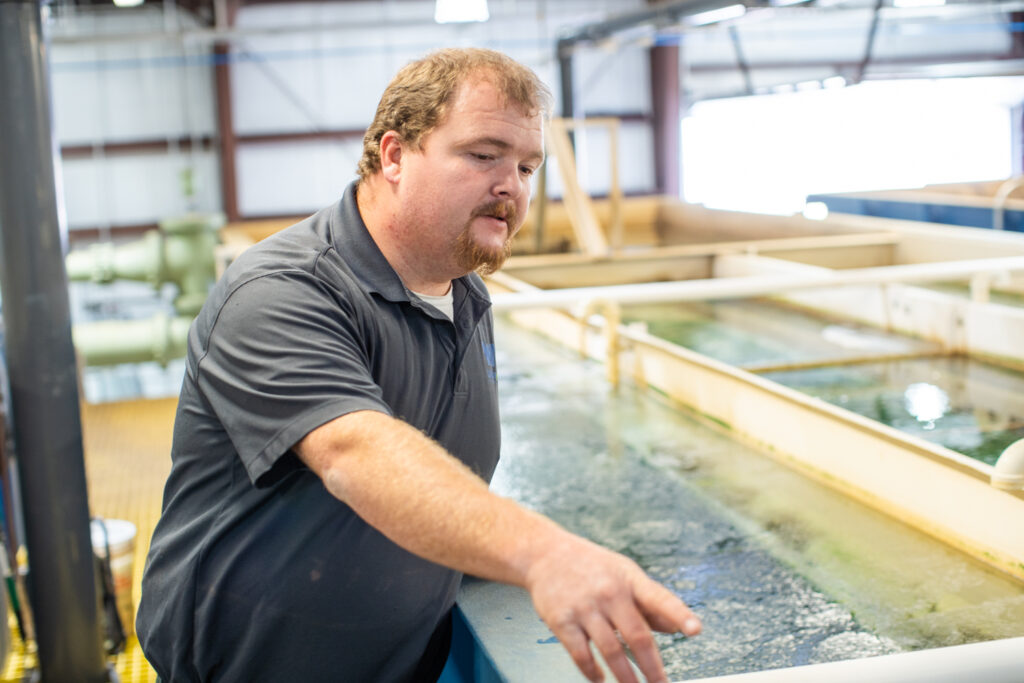 A Water Tech employee pointing at something off-screen. There are open tanks of water behind him.