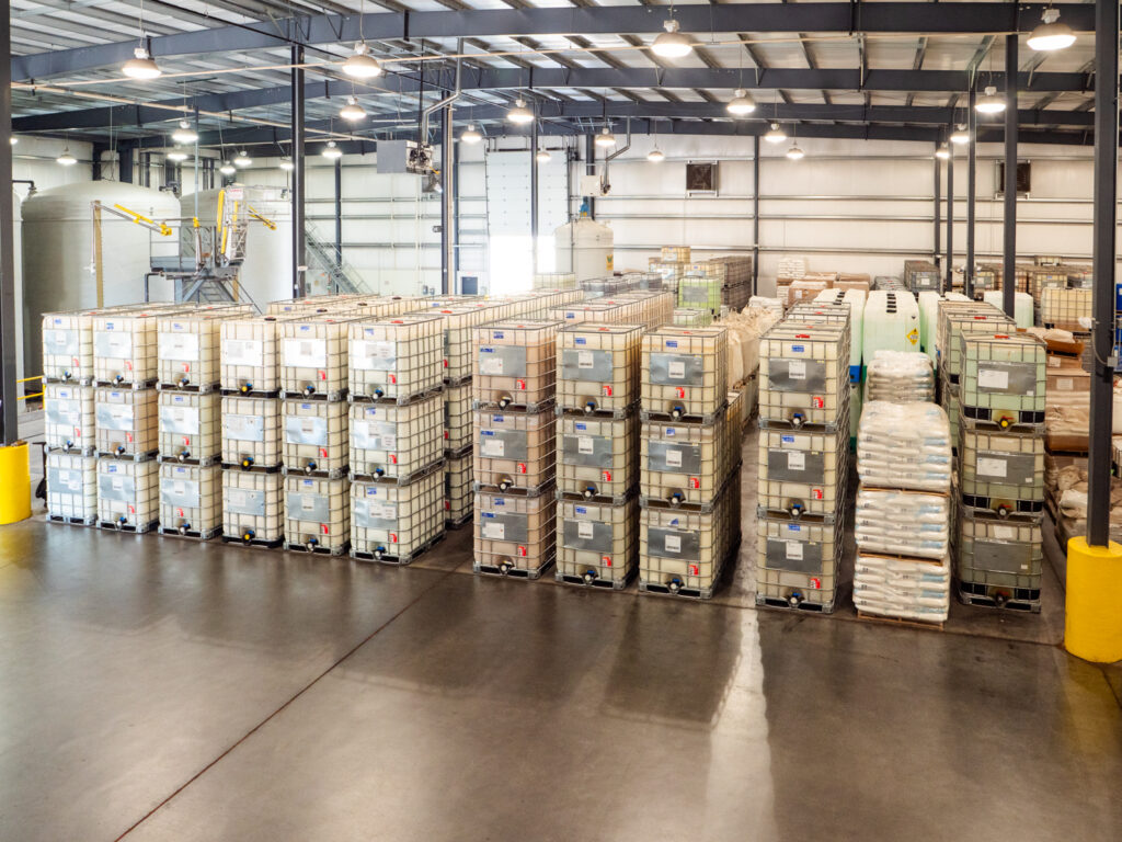 Stacks of square plastic chemical containers in wire boxes in rows in a Water Tech warehouse.