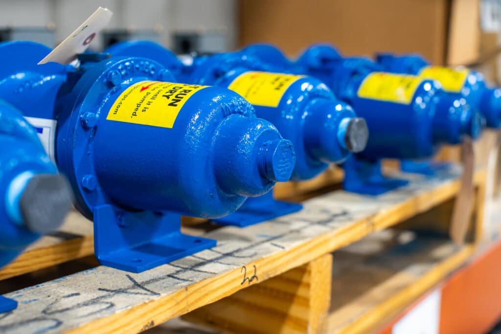 A row of five blue pump heads at Water Tech, Inc.. The pumps are shiny blue and there are bright yellow stickers on top.