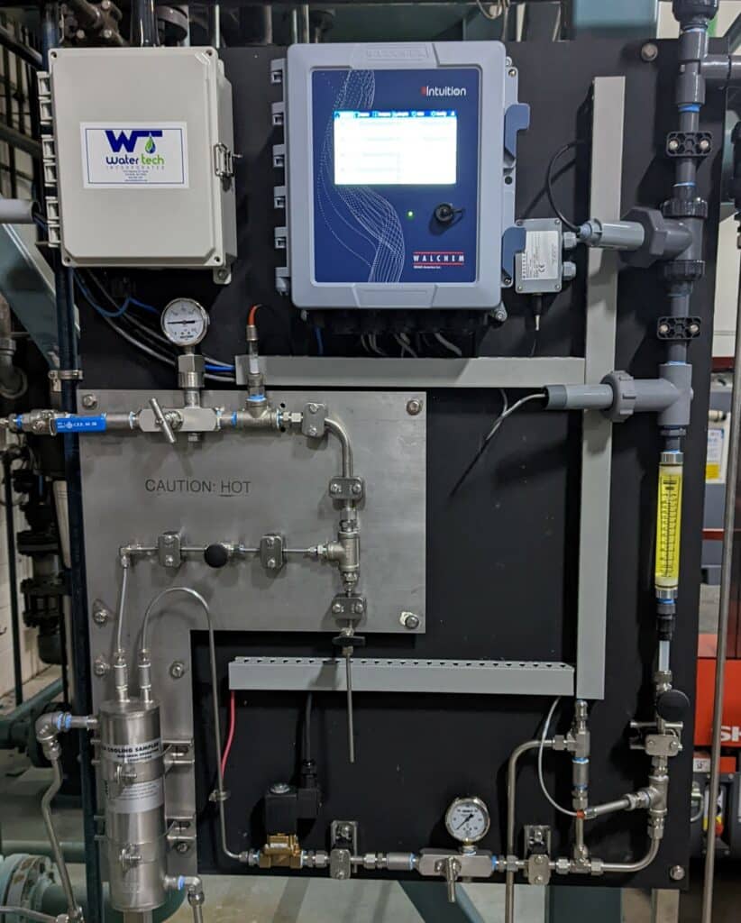 A black boiler panel with gray, metal tubes running along the sign and into a compression tank. The Water Tech sticker is on the control box.